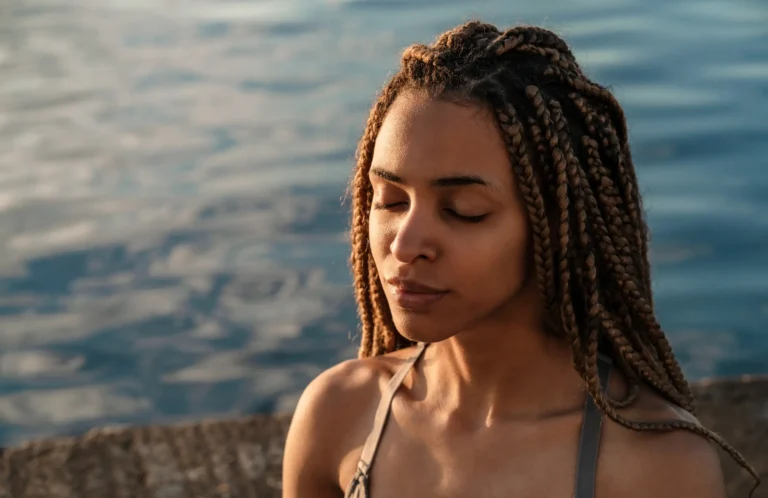 Woman meditating outdoors near water.