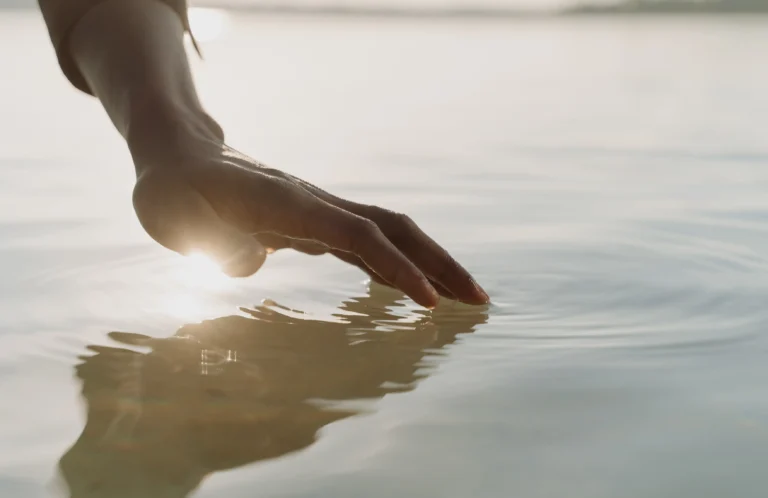 Hand touching calm water with gentle ripples